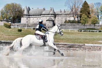 White horse galloping through water, in front of a traditionnal french chateau. 